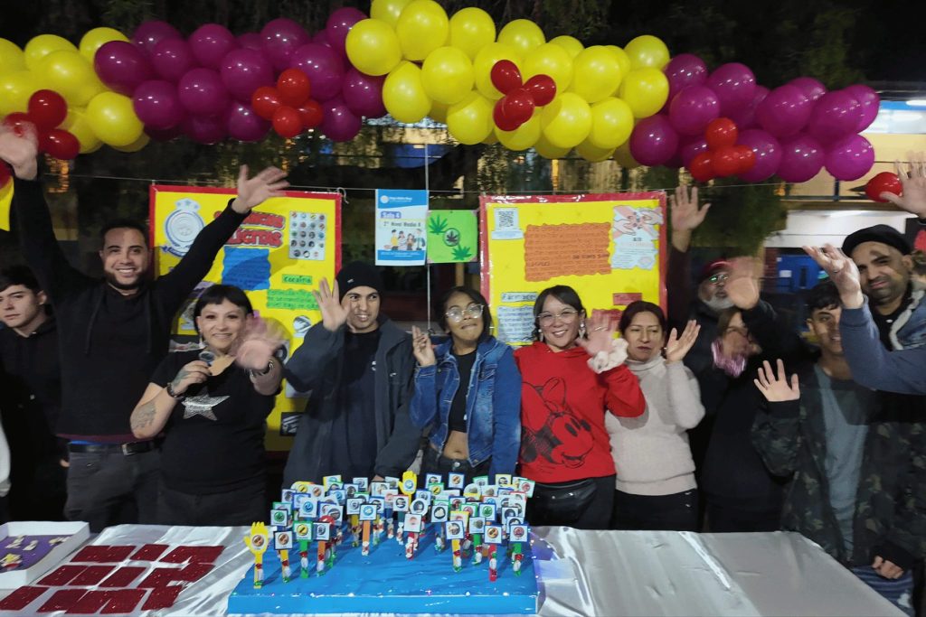 Curso de 2° Nivel Medio saludando junto a su stand con arco de globos